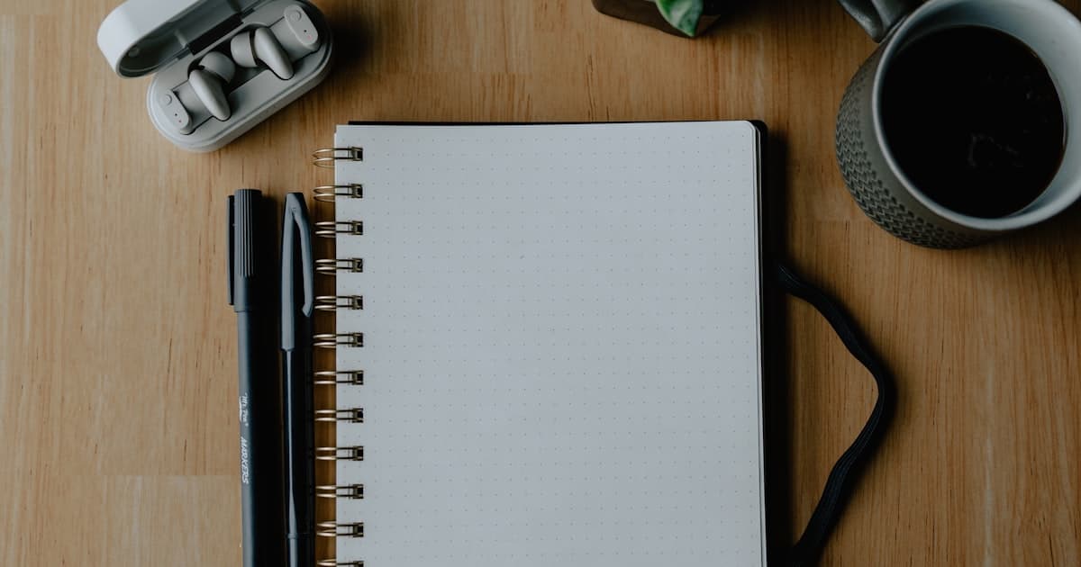 Notebook, pens, and coffee arranged on a wooden table