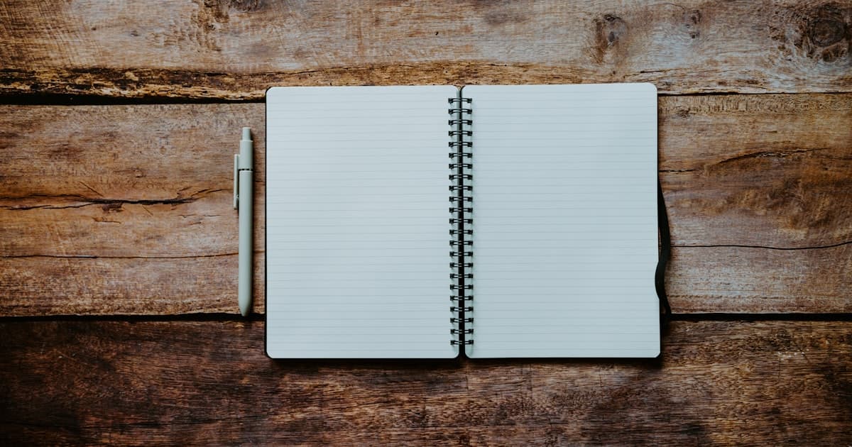 An open spiral-bound notebook and a pen on a rustic wooden table