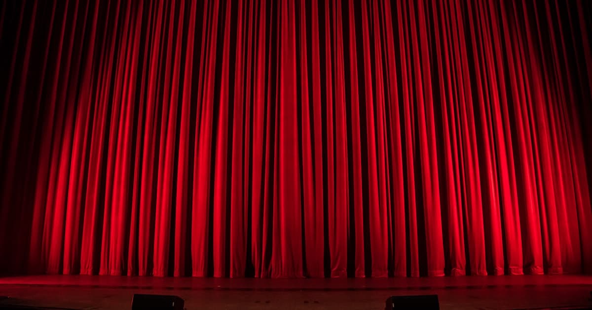 A red theater curtain under warm stage light