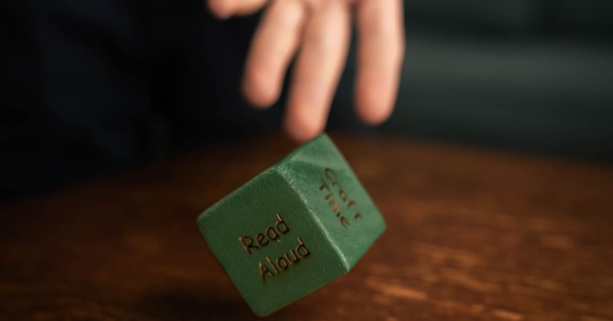 A hand tossing a green die onto a dark wooden game table