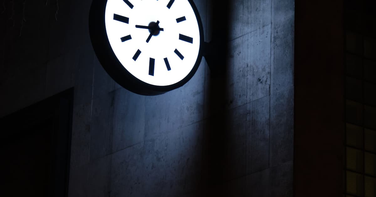 An illuminated analog clock mounted on a dark stone wall